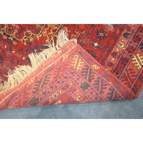 1280 - A RED GROUND RECTANGULAR WOOLEN RUG, with repeating geometric patterns, surrounded by a multi-strap ... 