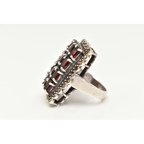 85 - A WHITE METAL GARNET SET DRESS RING, of a large rectangular form set with four rows of three oval cu... 