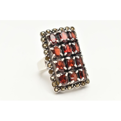 85 - A WHITE METAL GARNET SET DRESS RING, of a large rectangular form set with four rows of three oval cu... 