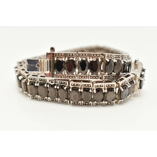 86 - A WHITE METAL GEM SET LINE BRACELET, set with a series of oval cut black stones, each in a four claw... 