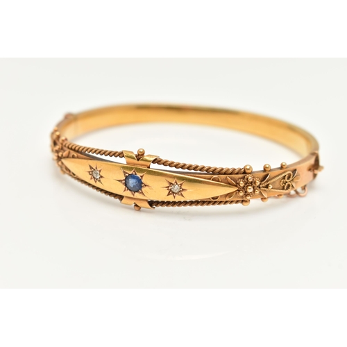 78 - A VICTORIAN YELLOW METAL GEM SET BANGLE, with a star set circular cut blue sapphire, flanked with tw... 