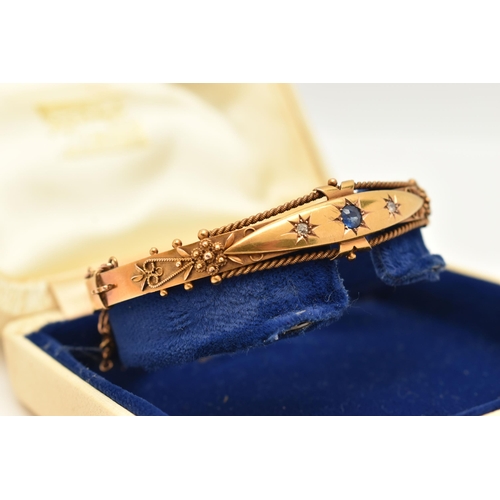 78 - A VICTORIAN YELLOW METAL GEM SET BANGLE, with a star set circular cut blue sapphire, flanked with tw... 