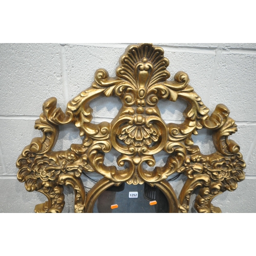 1252 - A MODERN ORNATE GILT FRAME WALL MIRROR, with scrolled and foliate details, a circular pane, above a ... 