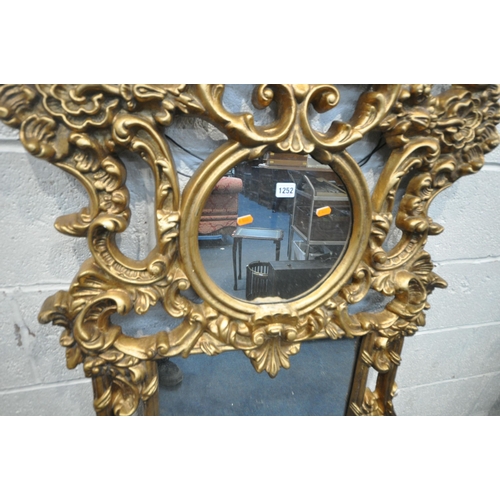 1252 - A MODERN ORNATE GILT FRAME WALL MIRROR, with scrolled and foliate details, a circular pane, above a ... 