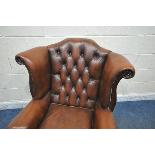 1242 - A TANNED BUTTONED LEATHER CHESTERFIELD WINGBACK ARMCHAIR, with scrolled armrests, raised on front ca... 