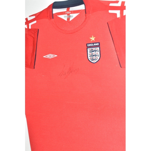 486 - A FRAMED ENGLAND FOOTBALL SHIRT, bearing signature, an official Umbro product red England Away footb... 