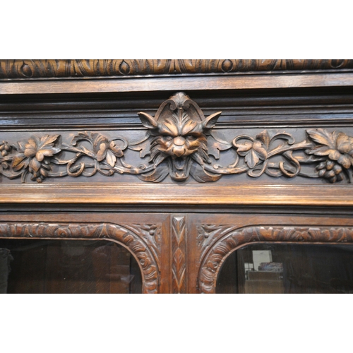 154 - A 20TH CENTURY OAK BOOKCASE, with intricate carved details, the double glazed doors enclosing three ... 