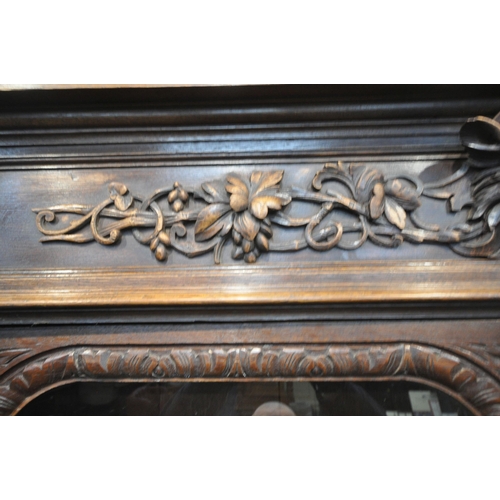 154 - A 20TH CENTURY OAK BOOKCASE, with intricate carved details, the double glazed doors enclosing three ... 