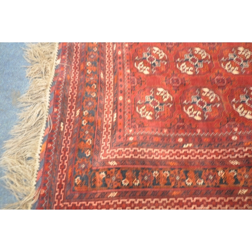 201 - A IRANIAN RED WOOLEN TEKKE RUG, with twelve central medallions, surrounded by a multi-strap border, ... 