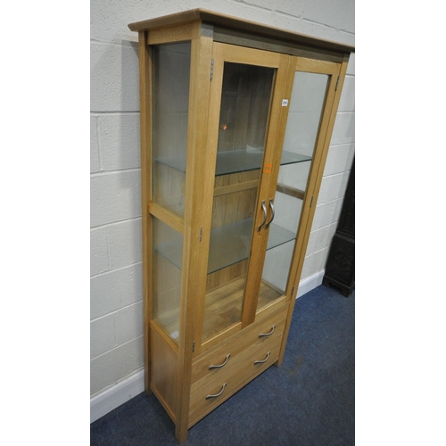 214 - A MODERN LIGHT OAK DISPLAY CABINET, with double glass doors, that are enclosing two glass shelves, a... 