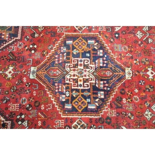 221 - A HAND WOVEN RED GROUND IRANIAN KASHGAI RECTANGULAR RUG, with repeating geometric patterns, surround... 