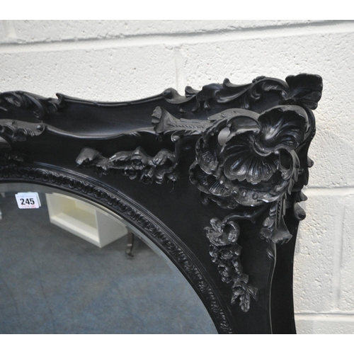 245 - A BLACK PAINTED RECTANGULAR WALL MIRROR, with ornate foliate details, surrounding an oval bevelled m... 