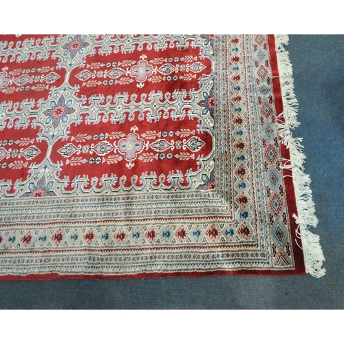 269 - A RED GROUND RECTANGULAR WOOLLEN RUG, with repeating foliate and geometric patterns, surrounded by a... 