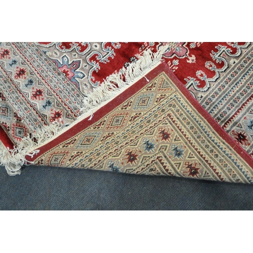 269 - A RED GROUND RECTANGULAR WOOLLEN RUG, with repeating foliate and geometric patterns, surrounded by a... 