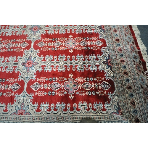 269 - A RED GROUND RECTANGULAR WOOLLEN RUG, with repeating foliate and geometric patterns, surrounded by a... 