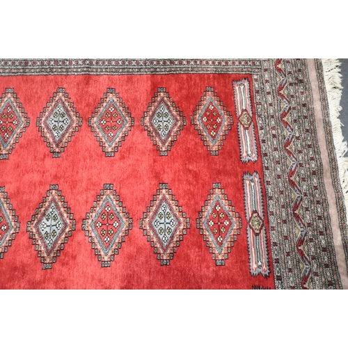 279 - A LARGE RED GROUND RECTANGULAR RUG, with forty-four central medallions, surrounded by a multi-strap ... 