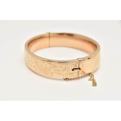 421 - A 9CT GOLD HINGED BANGLE, decorated to one side with a floral and foliate pattern, fitted with a pus... 