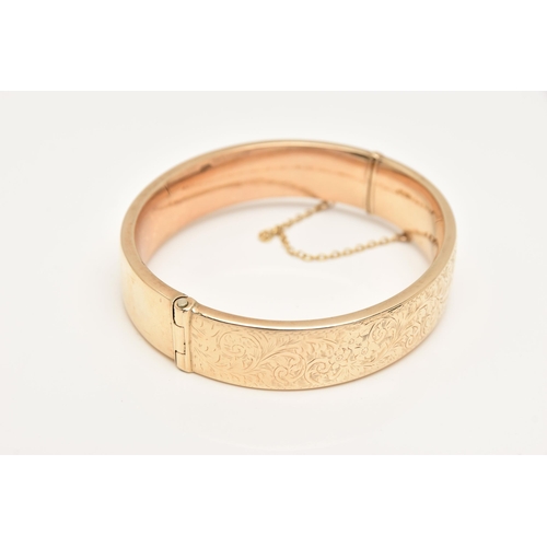 421 - A 9CT GOLD HINGED BANGLE, decorated to one side with a floral and foliate pattern, fitted with a pus... 