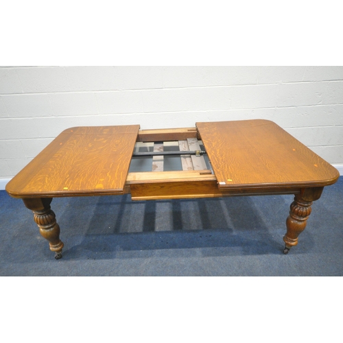 200 - A LARGE 20TH CENTURY OAK WIND OUT DINING TABLE, with three additional leaves, raised on reeded and t... 