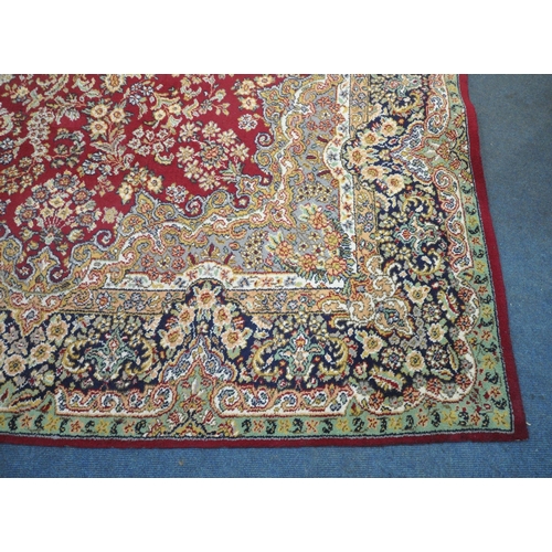 256 - A LARGE RECTANGULAR RED GROUND RUG, with repeating foliate and scrolled details, surrounded by a mul... 