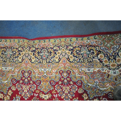 256 - A LARGE RECTANGULAR RED GROUND RUG, with repeating foliate and scrolled details, surrounded by a mul... 