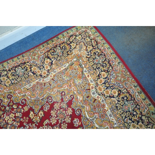 256 - A LARGE RECTANGULAR RED GROUND RUG, with repeating foliate and scrolled details, surrounded by a mul... 