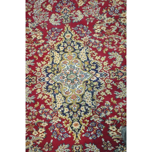 256 - A LARGE RECTANGULAR RED GROUND RUG, with repeating foliate and scrolled details, surrounded by a mul... 