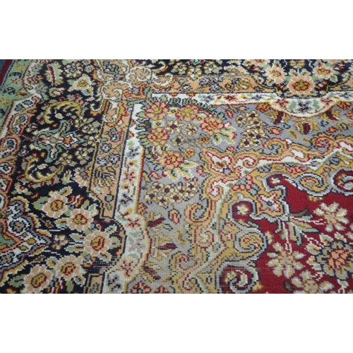 256 - A LARGE RECTANGULAR RED GROUND RUG, with repeating foliate and scrolled details, surrounded by a mul... 