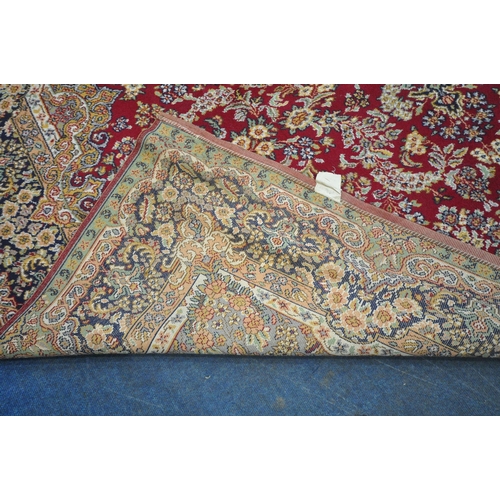 256 - A LARGE RECTANGULAR RED GROUND RUG, with repeating foliate and scrolled details, surrounded by a mul... 