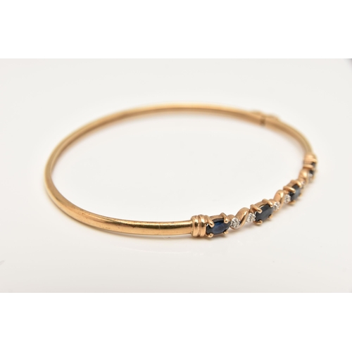 427 - A YELLOW METAL GEM SET BANGLE, set with four oval cut deep blue sapphires interspaced with illusion ... 