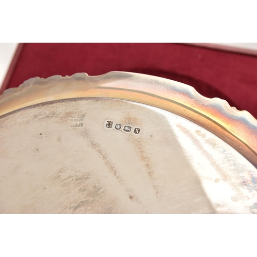 537 - A CASED ELIZABETH II SILVER PRESENTATION SALVER, circular form with wavy rim, engraving to the rever... 