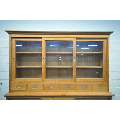 185 - A LARGE MODERN OAK HOUSEKEEPERS CUPBOARD, fitted with triple glass sliding doors, six drawers, atop ... 