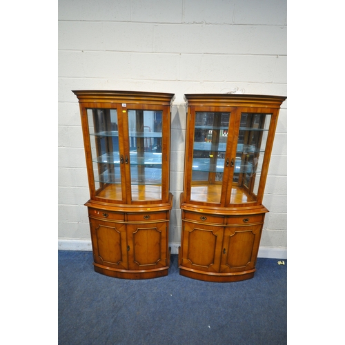 158 - A PAIR OF REPRODUCTION BOW FRONT YEW WOOD DISPLAY CABINETS, the double glazed doors enclosing a mirr... 