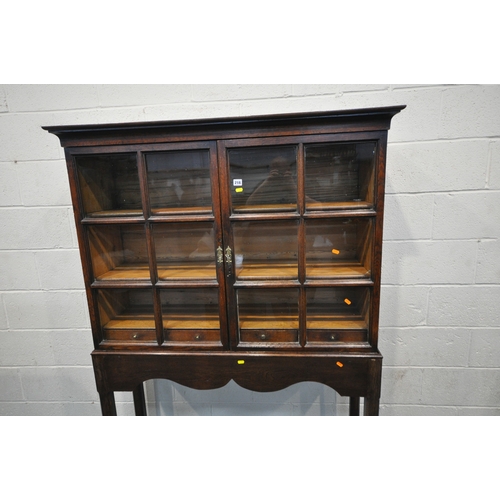 218 - AN OAK CABINET ON STAND, the double glass doors enclosing two shelves and four drawers, width 125cm ... 