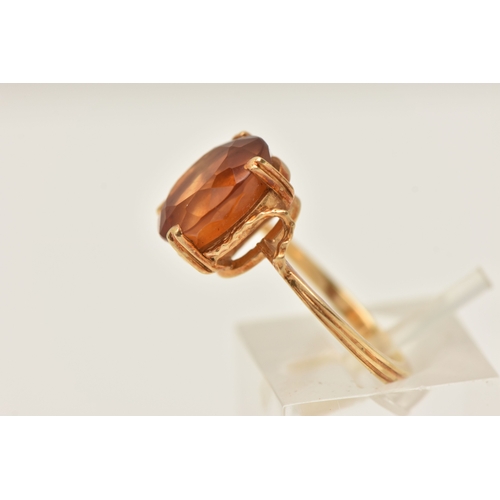 411 - A YELLOW METAL GEM SET RING, an oval cut deep orange brown Citrine, prong set in yellow metal, stamp... 