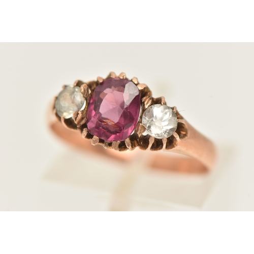 417 - A ROSE METAL GEM SET RING, AF set with a central oval cut garnet claw set and flanked with two circu... 