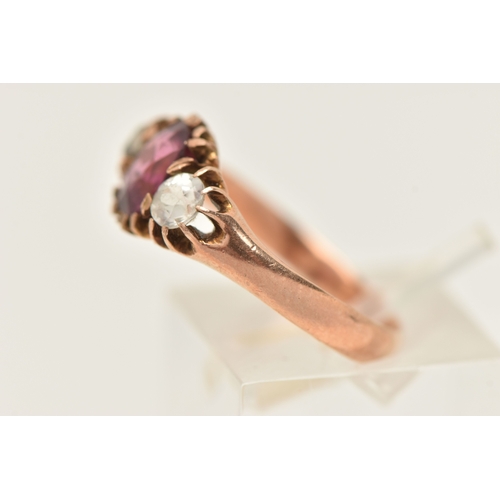 417 - A ROSE METAL GEM SET RING, AF set with a central oval cut garnet claw set and flanked with two circu... 