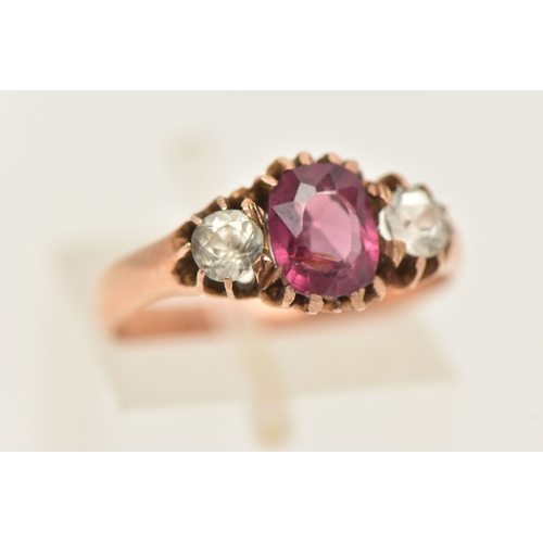 417 - A ROSE METAL GEM SET RING, AF set with a central oval cut garnet claw set and flanked with two circu... 