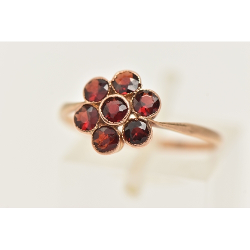 418 - A YELLOW METAL GARNET SET FLOWER RING, set with seven circular cut garnets, milgrain settings, to th... 