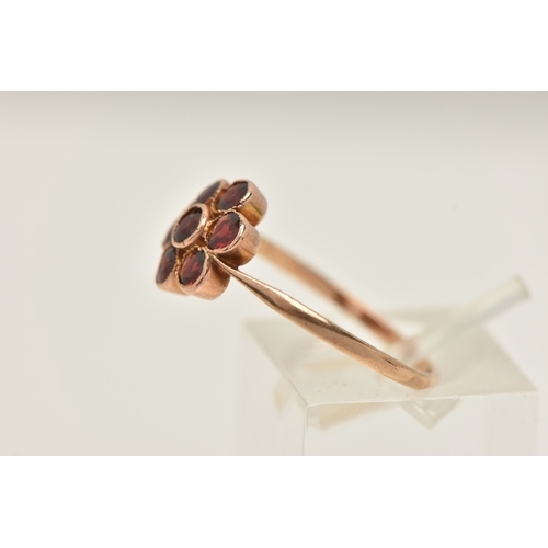 418 - A YELLOW METAL GARNET SET FLOWER RING, set with seven circular cut garnets, milgrain settings, to th... 