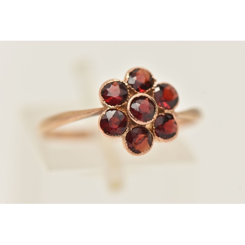 418 - A YELLOW METAL GARNET SET FLOWER RING, set with seven circular cut garnets, milgrain settings, to th... 