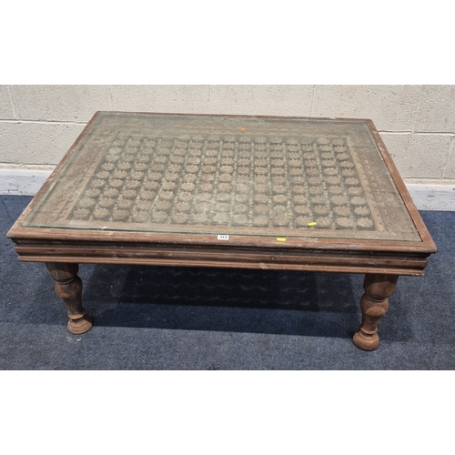 312 - A CARVED INDIAN RECTANGULAR COFFEE TABLE, with a glass insert, raised on block and turned legs, widt... 