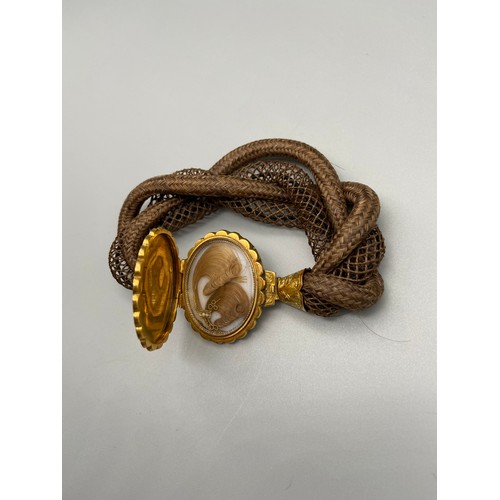 175J - A Victorian braided hair memorial bangle set with a large gold locket clasp. Locket contains two loc... 