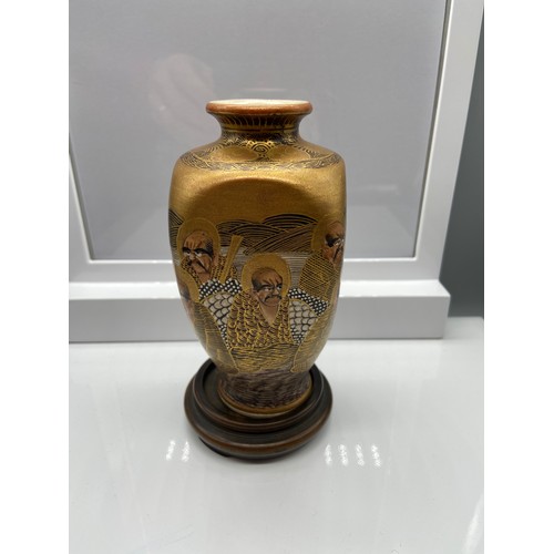 136 - A Japanese Satsuma hand painted vase with hard wood stand. Designed with figures, dragon and gilt tr... 