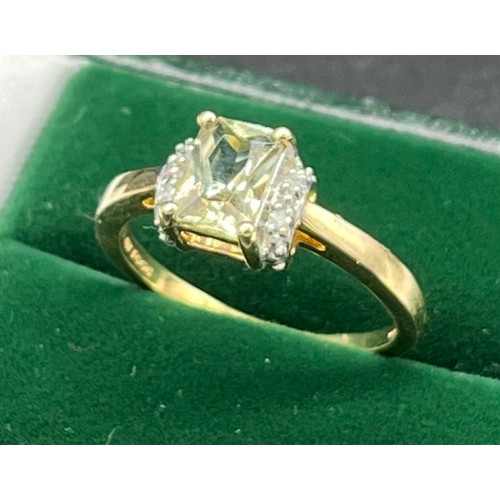 512 - 10ct yellow gold ladies ring set with and Emerald cut pale green topaz stone off set by diamond shou... 