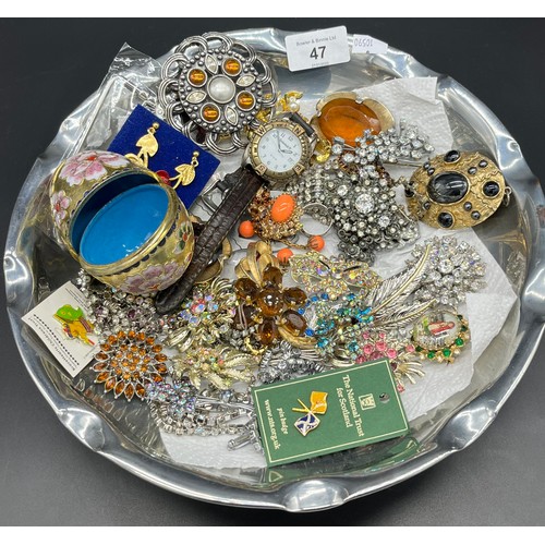 47 - Dish containing a quantity of costume jewellery items, brooches, cliosonne egg and Timberland watch.