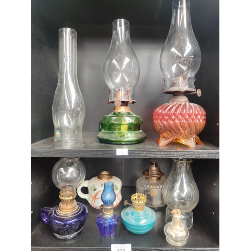 432 - Two shelves of antique glass oil lamps and shades and shelf of brass oil lamp burners and wicks.