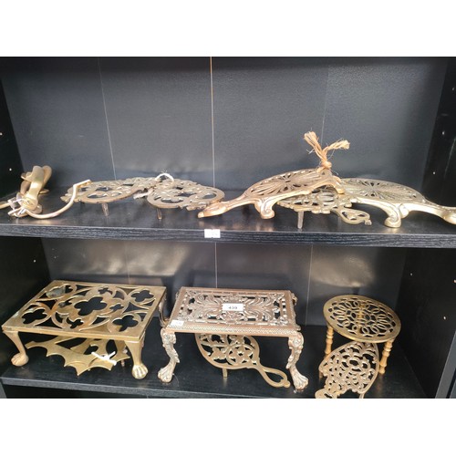 439 - Two shelves of antique brass trivet stands and resting plates.