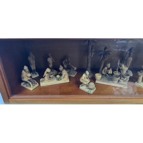 1358 - Wood and glass display case containing a collection of Nigerian Life Wooden carved miniature figures... 