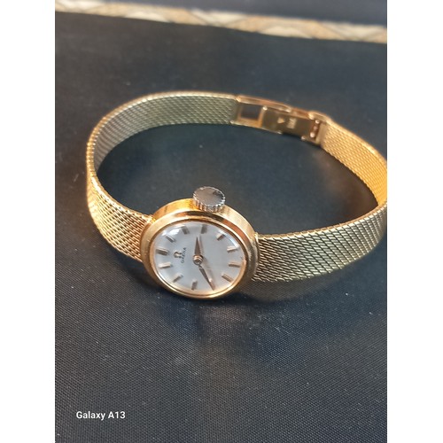 557 - Omega – a lady’s 18ct gold wristwatch, champagne dial, baton indicators, with an integral Milanese t... 